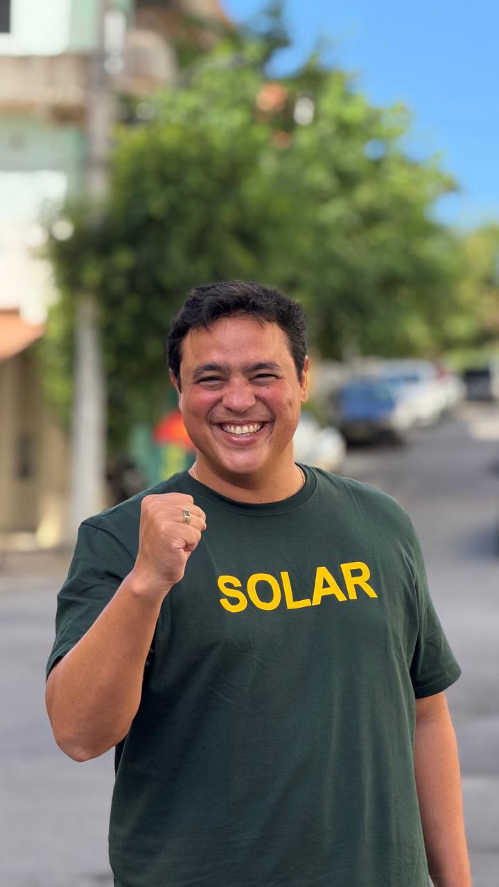 Marcos Rêgo sorrindo, com punho erguido, vestindo camiseta verde com a palavra SOLAR